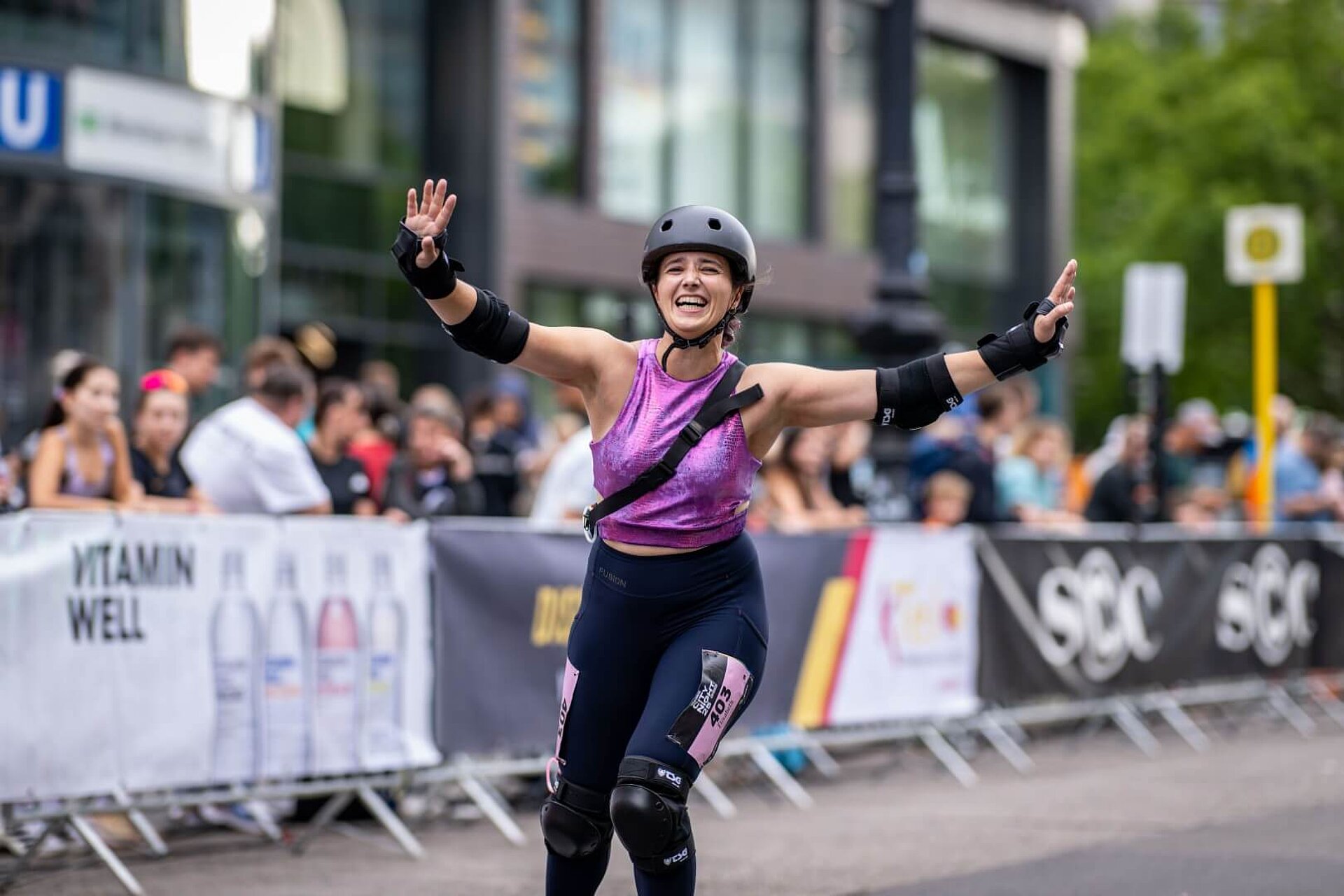 An enthusiastic inline skater with arms raised high skates on the track.