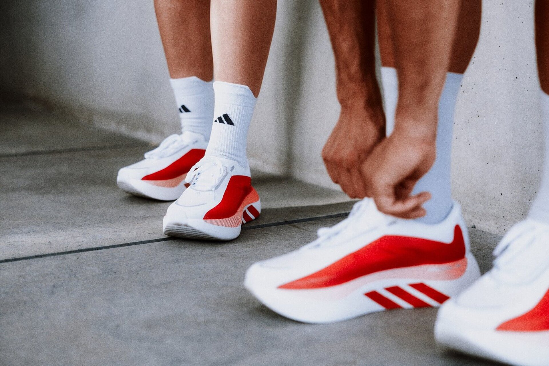 Vier Füße in weißen adidas Laufschuhen mit roten Akzenten.