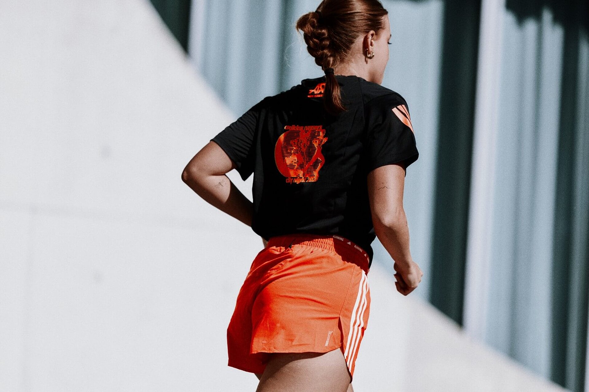 Läuferin von hinten in schwarzem T-Shirt mit orangenen Akzenzen und orangenen Shorts, beides von adidas.
