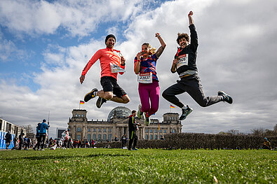 Three finishers jumping for joy on the Reichstags lawn